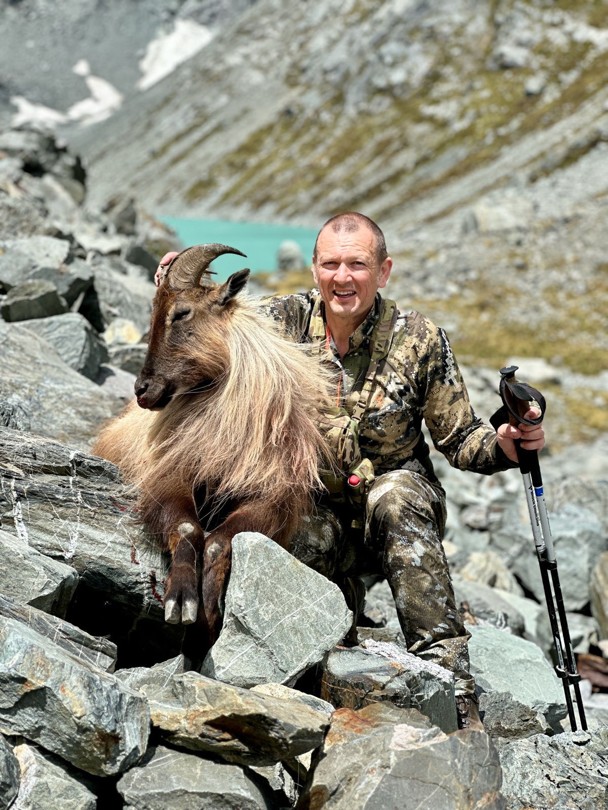 the developer on a boulder field beside a glacier-fed tarn with a bull tahr he has taken.
